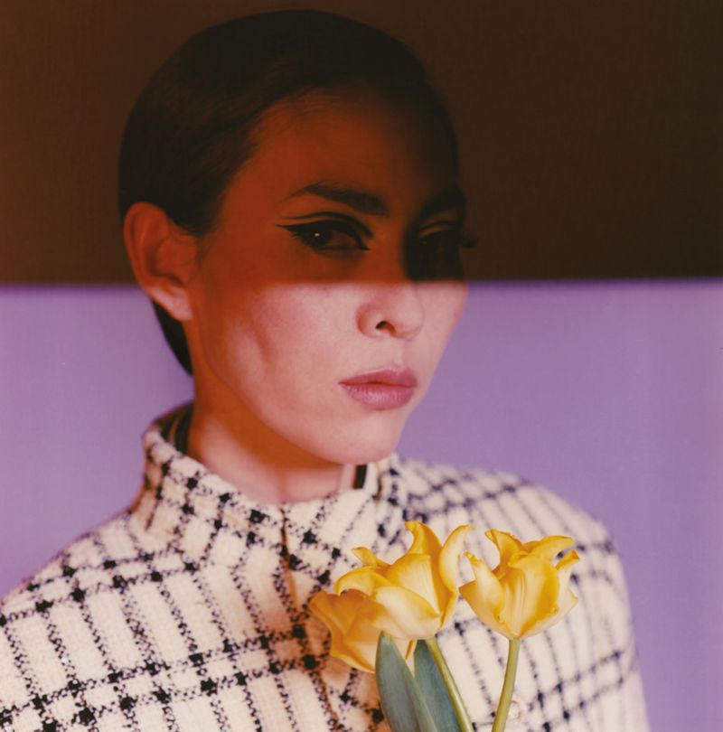 Elegant woman poses with yellow tulips in front of a purple background.  The image features a modern editorial fashion style.