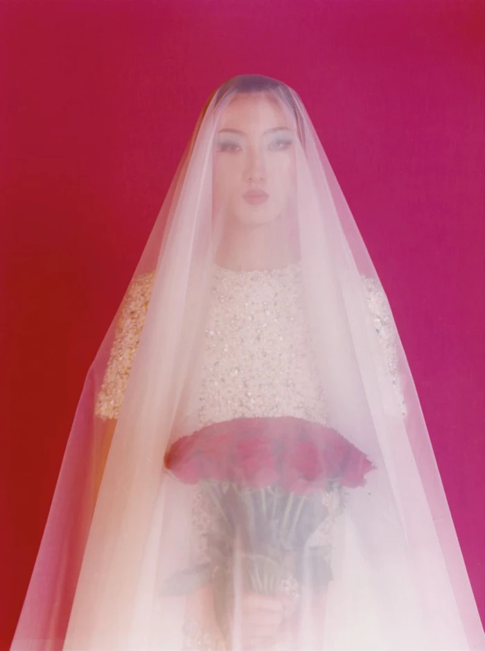 Model wearing a white veil holding red roses against a solid pink background for The Face Magazine