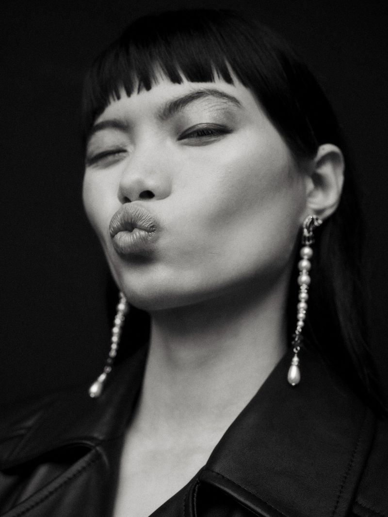 Close-up black and white portrait of model Chun Jin pouting with long pearl drop earrings and a leather jacket.