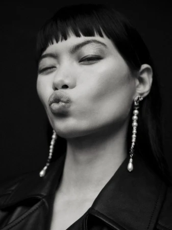 Close-up black and white portrait of model Chun Jin pouting with long pearl drop earrings and a leather jacket.