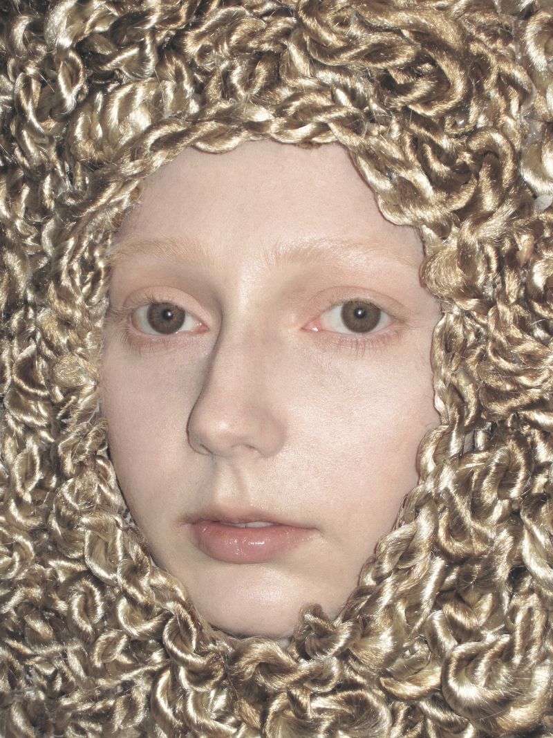 Close-up portrait of a woman wearing a textured metallic gold knitted hood framing her face