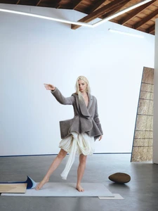 Anya Taylor-Joy in a grey jacket and white skirt posing barefoot in a minimalist white studio for an Elle UK editorial