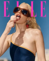 Chloe Cherry wearing oversized sunglasses and a navy swimsuit while licking an ice cream cone against a clear blue sky.