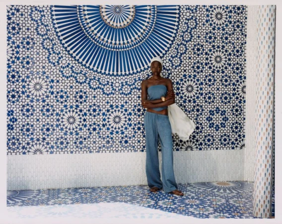 Model in a blue strapless top and matching wide-leg trousers standing against an ornate blue and white geometric tile wall.