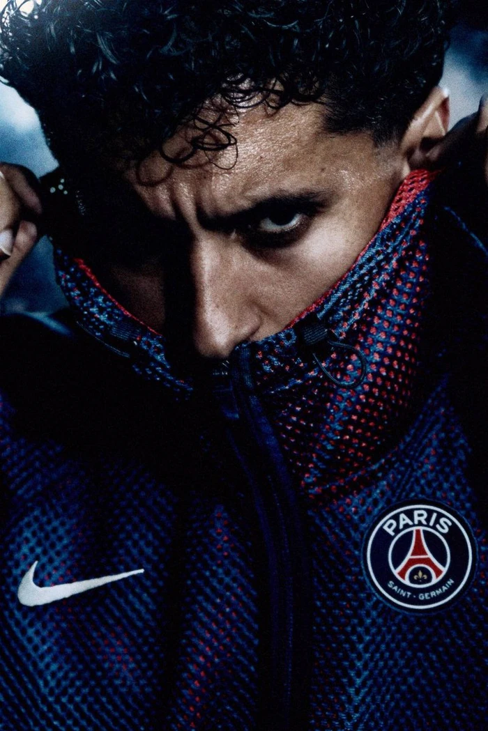 Close-up portrait of soccer player Marquinhos wearing a zipped Nike Paris Saint-Germain jacket pulled over his lower face.
