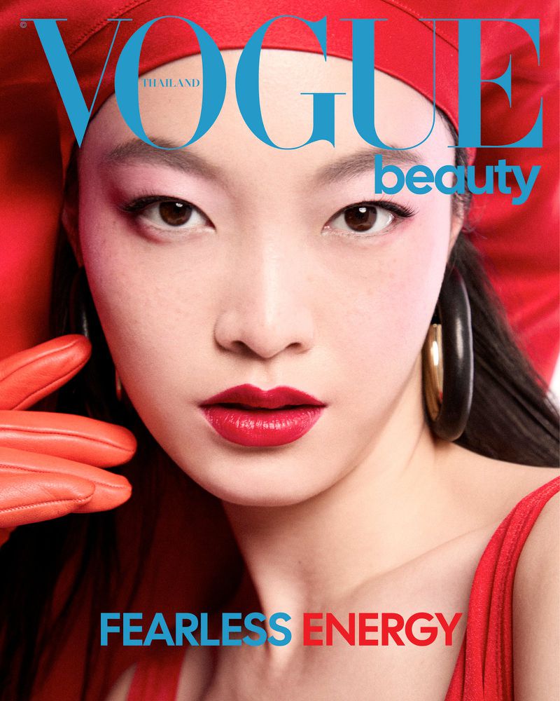 Close-up of an East Asian model with bold red lips wearing a red headscarf, bright orange gloves, and large black hoop earrings.