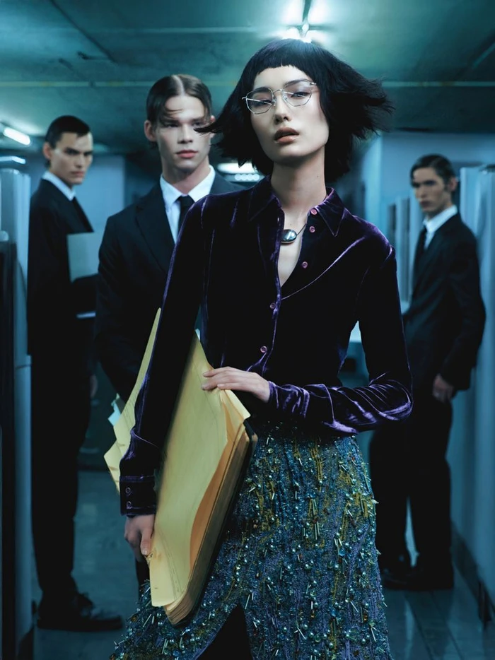 Woman in purple velvet shirt holding folders with three men in suits standing in background
