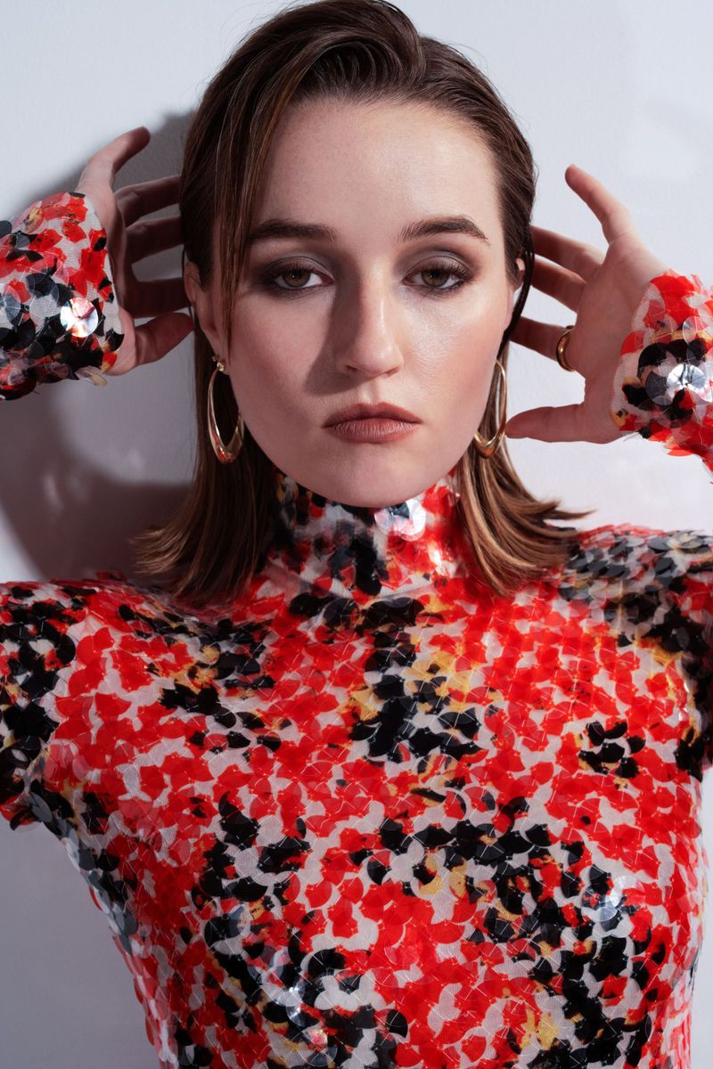 Close-up of a woman with wet hair, hoop earrings, and a vibrant patterned top against a white background in a beauty studio shot.