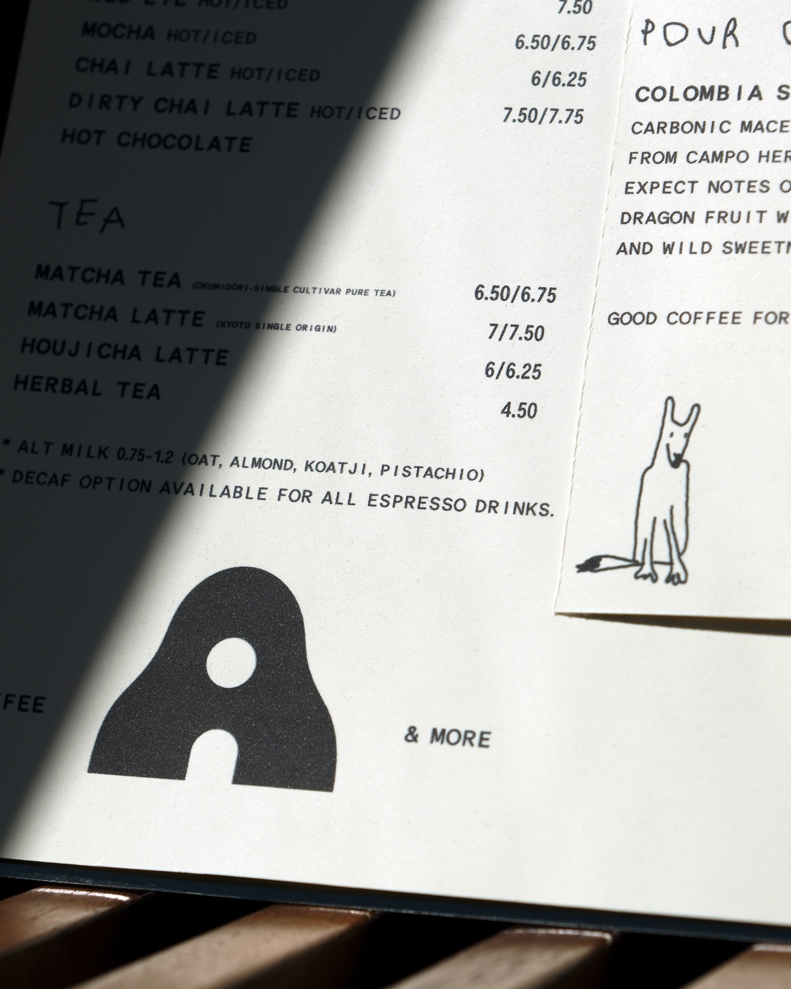 Printed Ants Coffee menu card with black typography and an illustrated dog slip casting a sharp diagonal shadow.