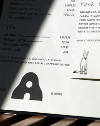 Printed Ants Coffee menu card with black typography and an illustrated dog slip casting a sharp diagonal shadow.