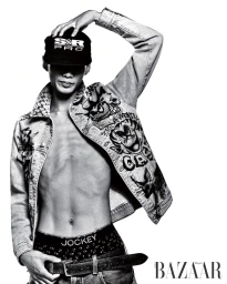Black and white studio portrait of model Bojvck Kang wearing an open graphic denim jacket, black cap, and low-slung jeans.