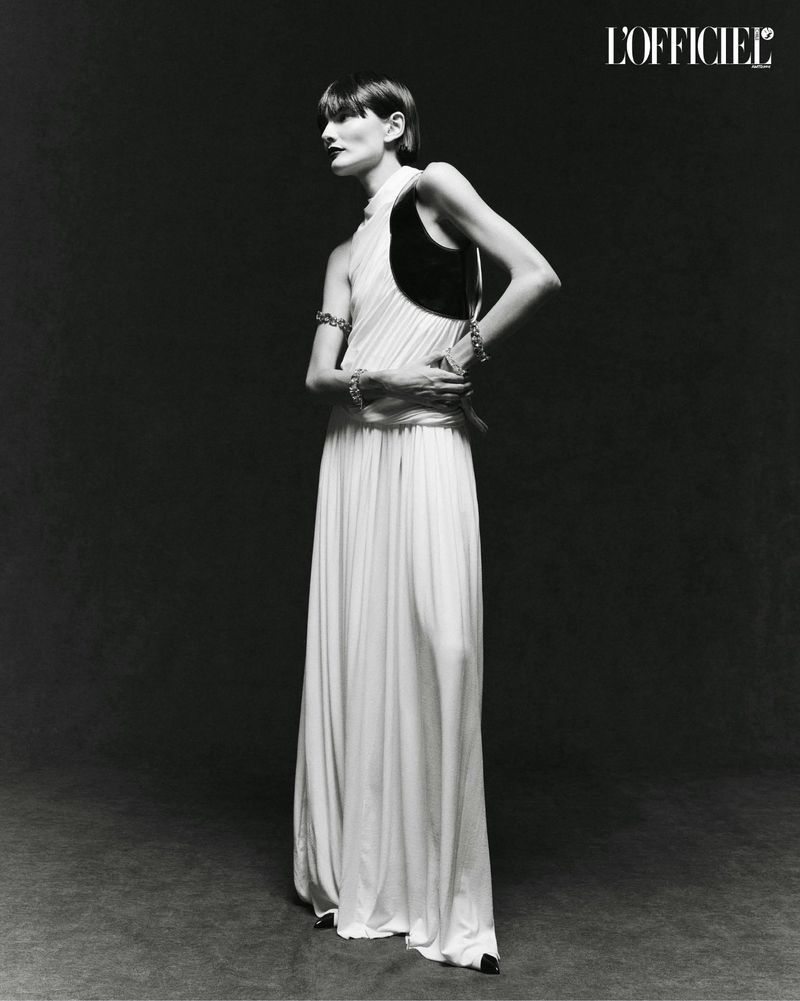 A full-length black-and-white portrait of a woman in a sleeveless gown, accessorized with bracelets, against a dark background.