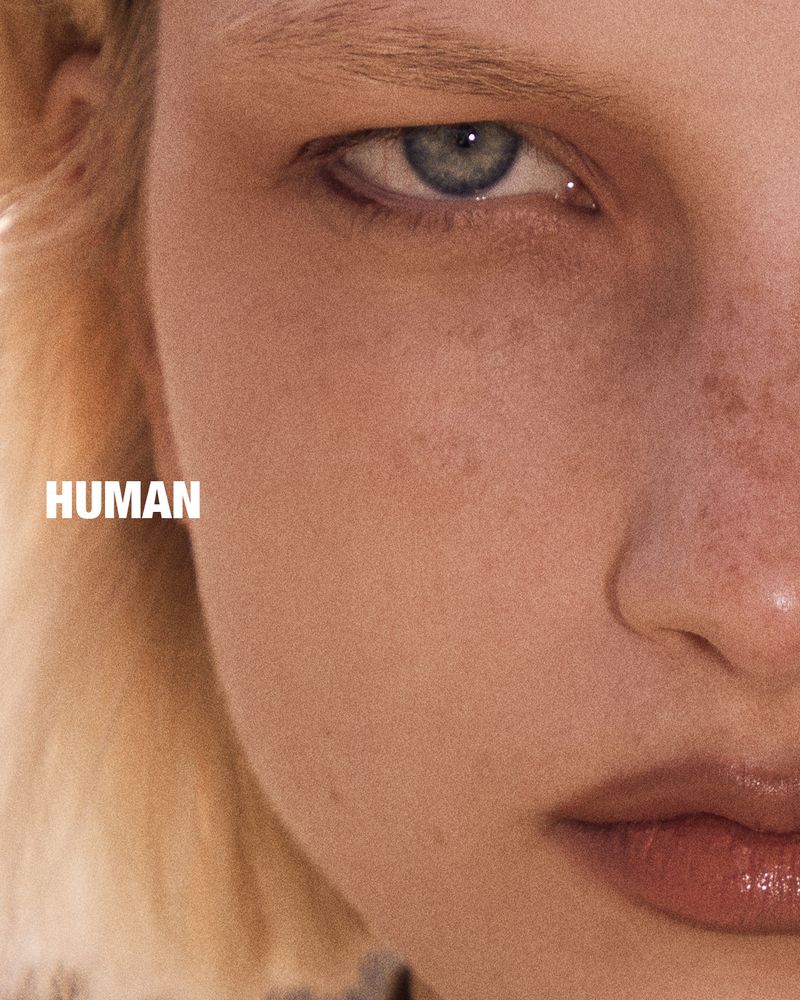 Close up portrait of a person with blonde hair, pale skin with freckles, and a blue eye, with the word HUMAN printed on the left side.