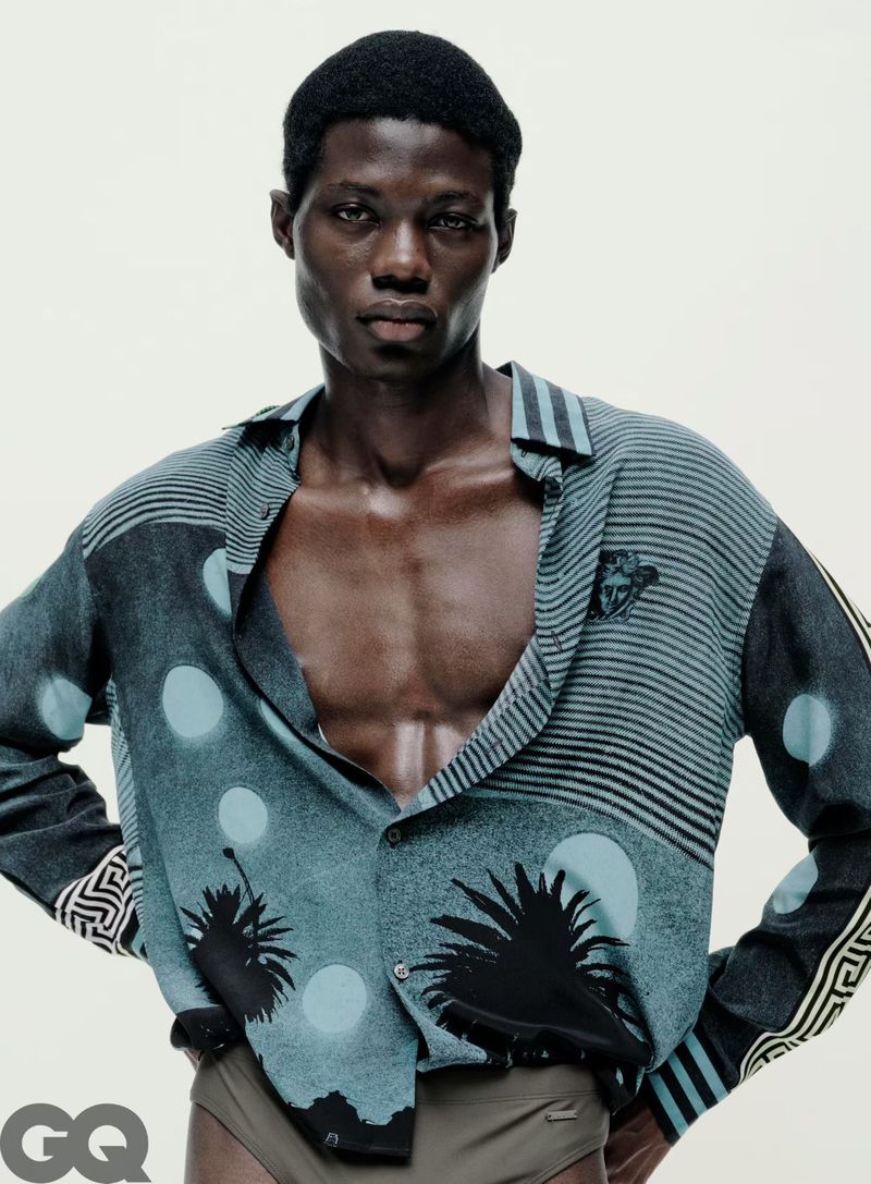 Model Lekan Bakare wearing an unbuttoned printed teal shirt and briefs against a white background for GQ China.