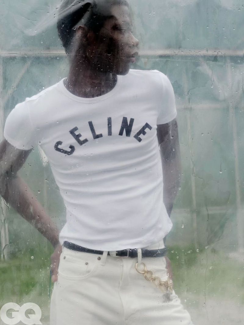 Model Lekan Bakare wearing a white Celine graphic t-shirt and white jeans viewed through rain-streaked glass.