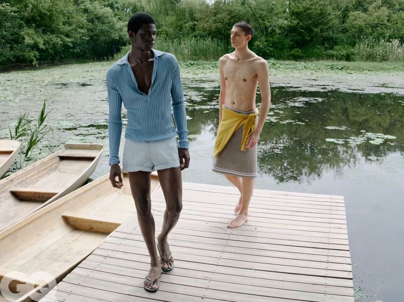 Lekan Bakare in a light blue ribbed long-sleeve polo and shorts walking on a wooden dock beside a lake.