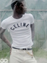 Model Lekan Bakare wearing a white Celine graphic t-shirt and white jeans viewed through rain-streaked glass.