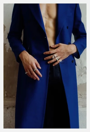 Model Francisco Rosso wearing an open royal blue tailored coat with silver rings over bare chest.