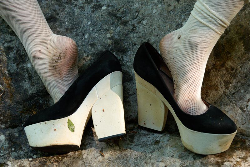 Close up of feet in white fishnet socks wearing black and white platform heels, resting on a rough grey rock surface.