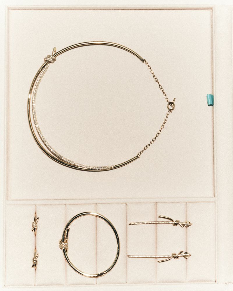 Gold and diamond knot jewellery set including a collar necklace, bracelet, earrings, and rings arranged in a pale velvet tray.