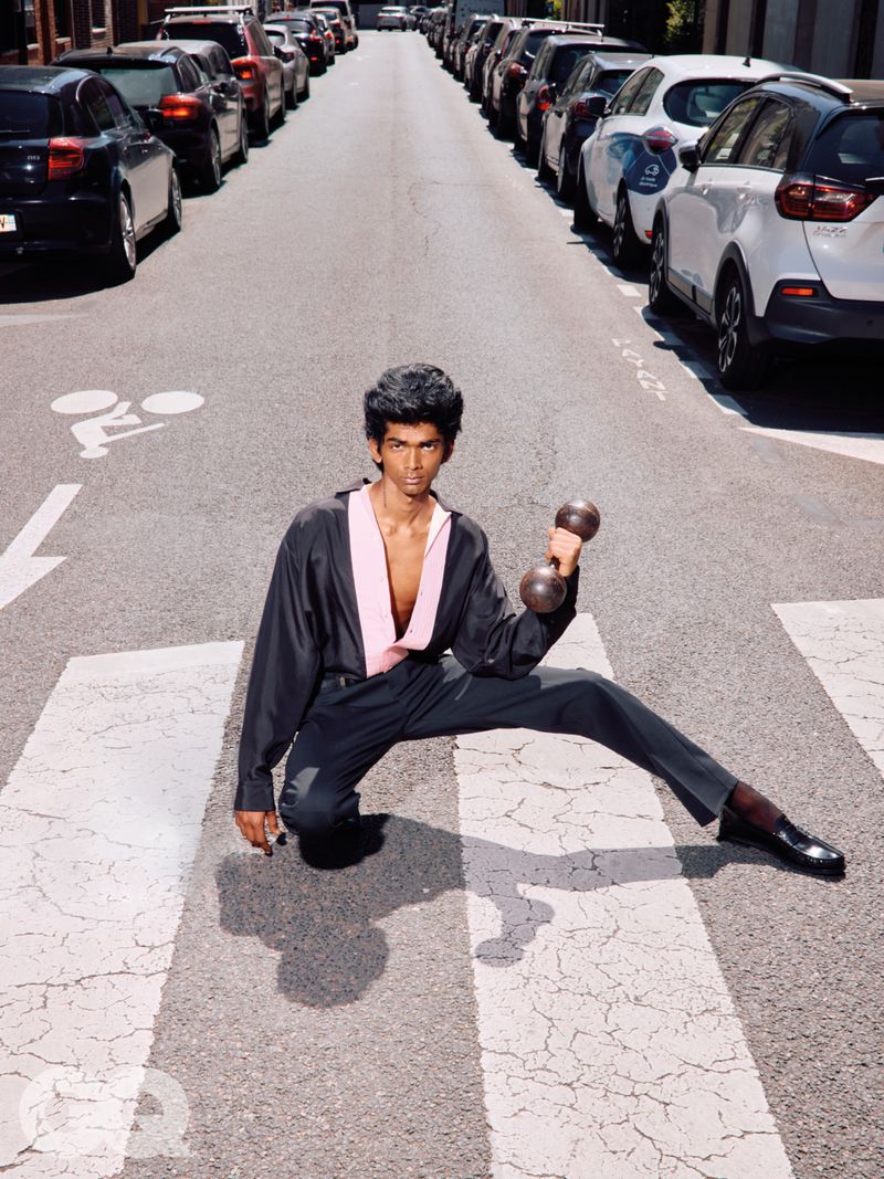 Man in a black and pink shirt kneeling in a street crosswalk while holding a dumbbell