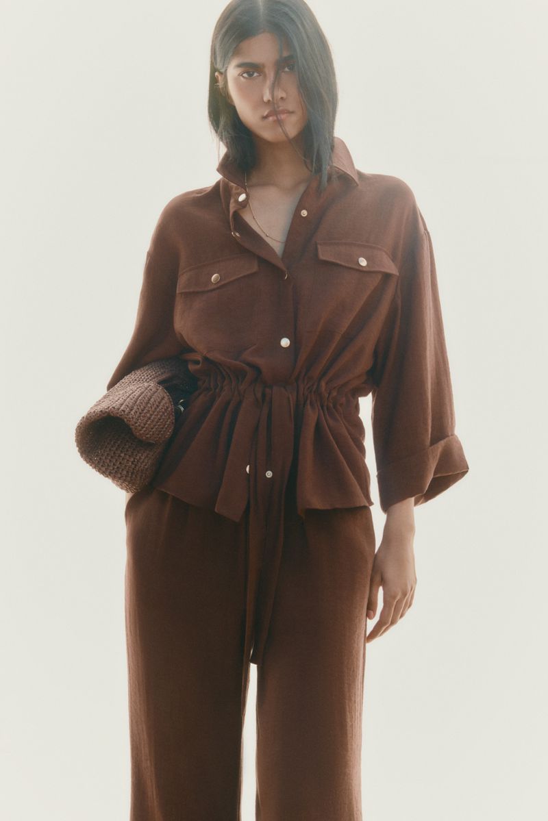 Model Ashley Radjarame wearing a monochromatic brown shirt and matching trousers against a bright studio backdrop.