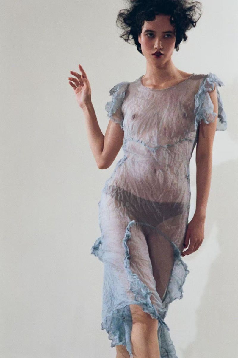 Model Yidan Huang wearing a sheer crinkled light blue ruffled dress against a plain studio background.