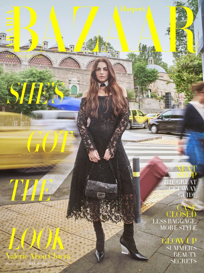 Valérie Abou Chacra wearing an off-the-shoulder black lace dress and pointed-toe heels standing on a city street crossing.
