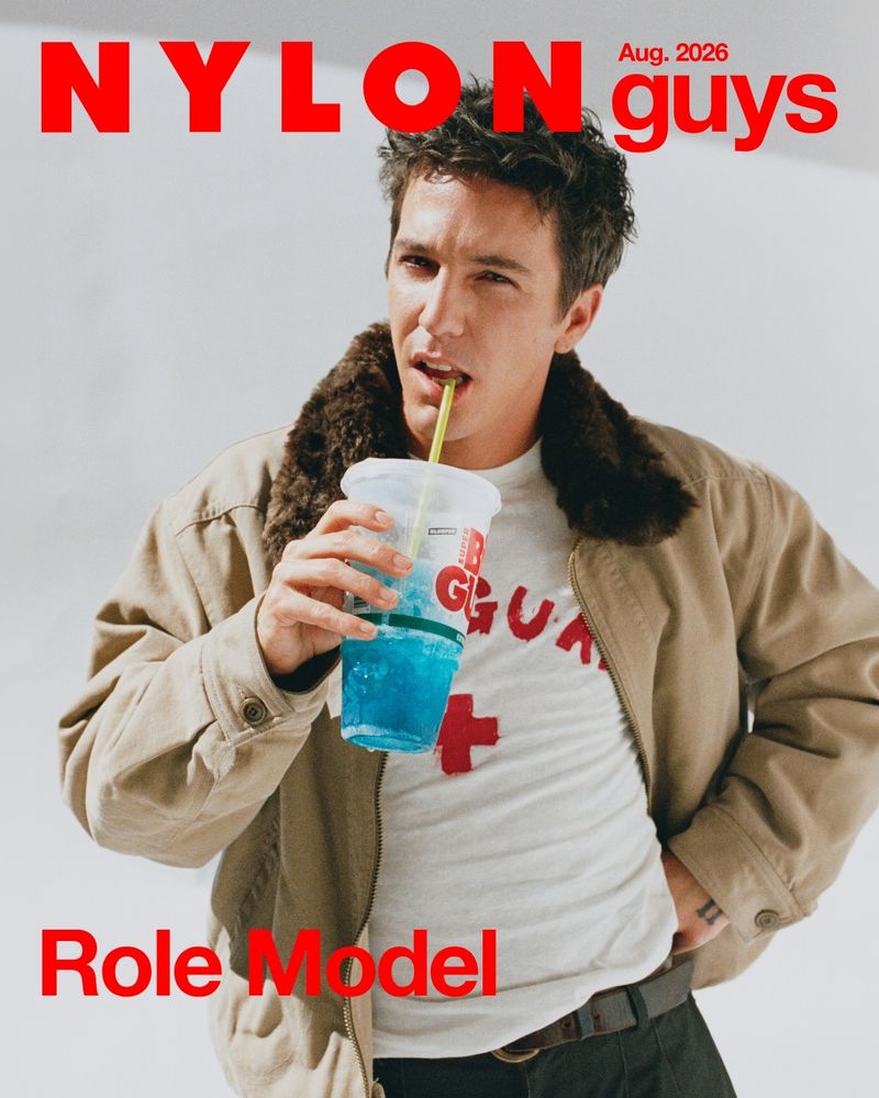 Role Model posing for the Nylon Guys cover wearing a tan shearling-collar jacket while sipping a blue slushie drink.