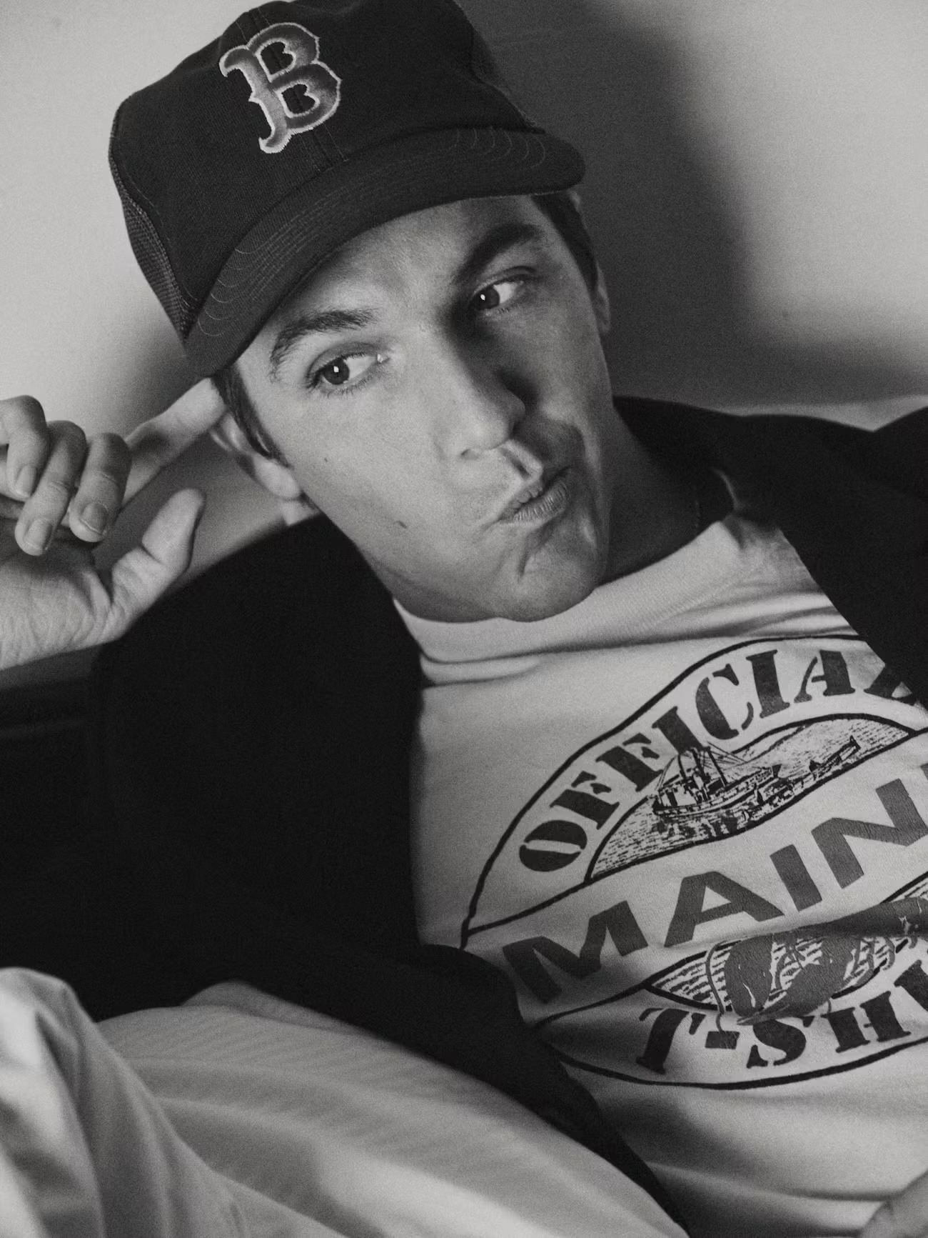 Black and white portrait of Role Model wearing a Boston Red Sox cap and graphic tee while reclining and making a playful expression.