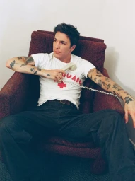 Role Model seated in a burgundy armchair holding a vintage corded telephone for Nylon Guys editorial shoot.