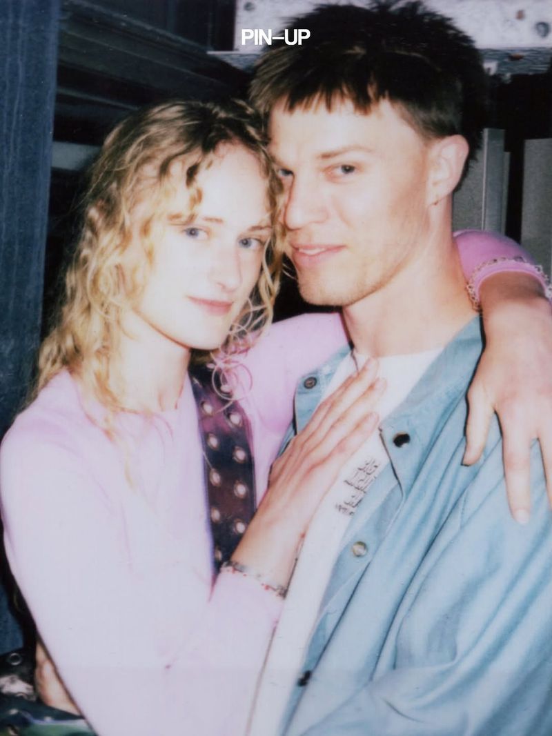 A woman with blonde curly hair in a pink top embracing a man in a light blue overshirt for PIN-UP Magazine.