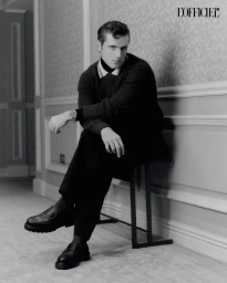 Man seated on a metal bench wearing a dark ribbed sweater and trousers in an editorial shot for L'Officiel Chile.
