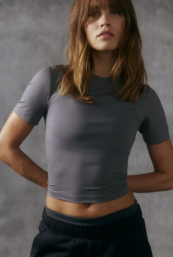 Model wearing a grey athletic t-shirt and black sweatpants against a textured concrete wall background
