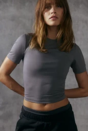 Model wearing a grey athletic t-shirt and black sweatpants against a textured concrete wall background