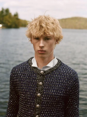 Blonde male model in a navy tweed buttoned jacket over a white shirt against a calm lake background.