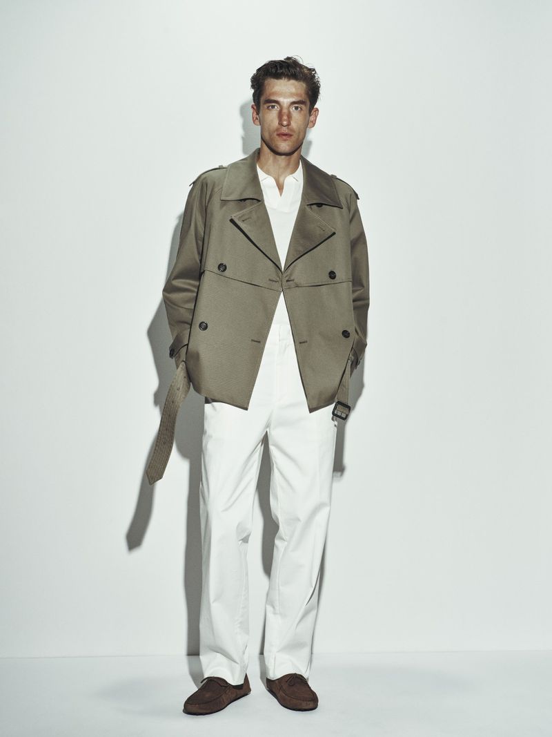 Full-length shot of a light-skinned adult male model wearing a beige jacket, white shirt and pants, and brown shoes against a white background.