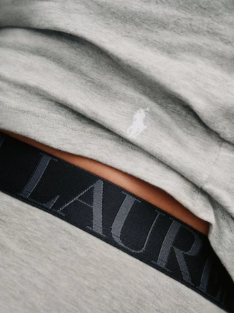 Close-up detail of grey heather cotton shirt with embroidered pony logo above a black branded elastic waistband.