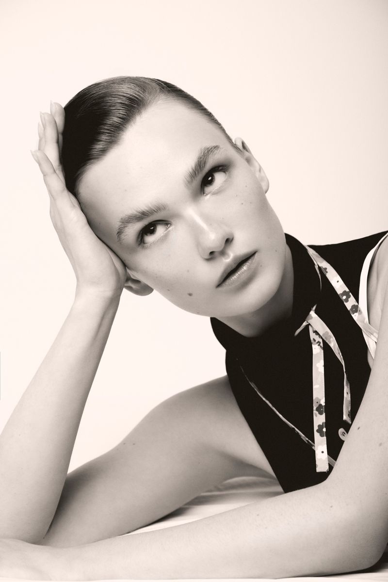 Close-up portrait of a woman resting her head on her hand while looking upward against a plain white studio backdrop.