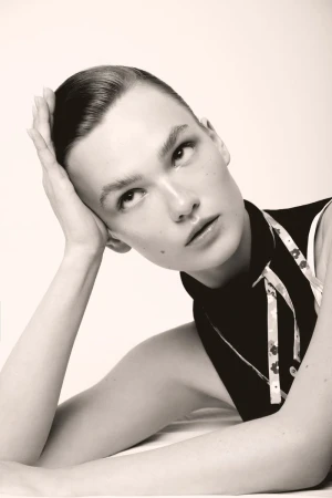 Close-up portrait of a woman resting her head on her hand while looking upward against a plain white studio backdrop.