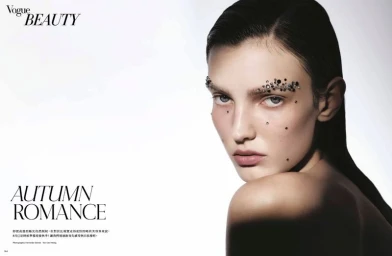 Woman looking over her shoulder with crystal-embellished eyebrows and face gems against a bright white background for Vogue Beauty.