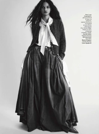 Model in dark cardigan over white blouse and voluminous denim skirt against seamless white