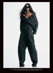 Model Ana Elisa Brito wearing an off-the-shoulder dark denim jacket and oversized wide-leg jeans with sunglasses against a white background.