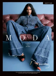 Model Ana Elisa Brito wearing an oversized denim shirt and wide-leg jeans seated on a tufted leather couch for Vanity Fair Italia.