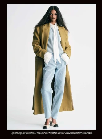 Model Ana Elisa Brito posing in a long mustard coat, light wash denim jeans, and a white ruffle blouse against a white background.