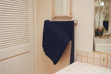 Dark navy long-sleeve knit draped over a chrome towel bar in a cream tiled bathroom beside a vanity counter.