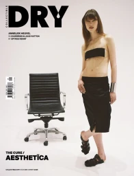 Model Anneliek Heuvel wearing black bandeau and skirt standing beside a black office chair in studio