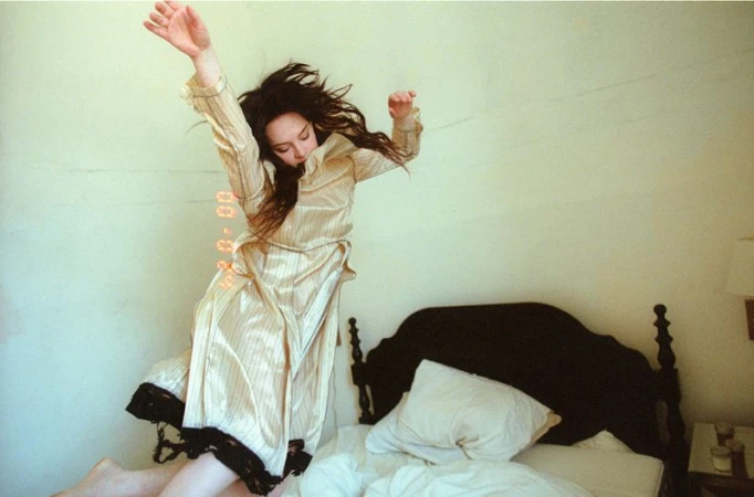 Sophie Thatcher jumping on a bed wearing a striped dress for i-D Magazine