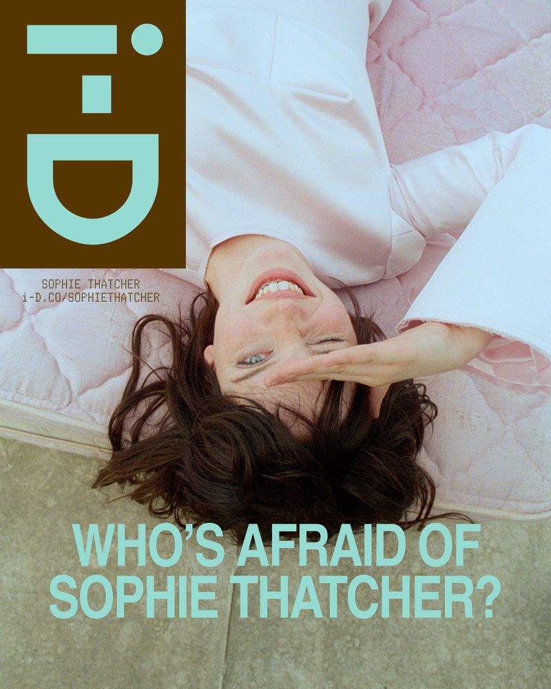 Sophie Thatcher lying on a pale pink quilted surface with a light-colored top, shading her eyes with one hand.