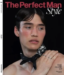 Male model Gabo Dos Santos with dewy makeup and bare shoulders wearing a black patterned neck scarf against a black backdrop.